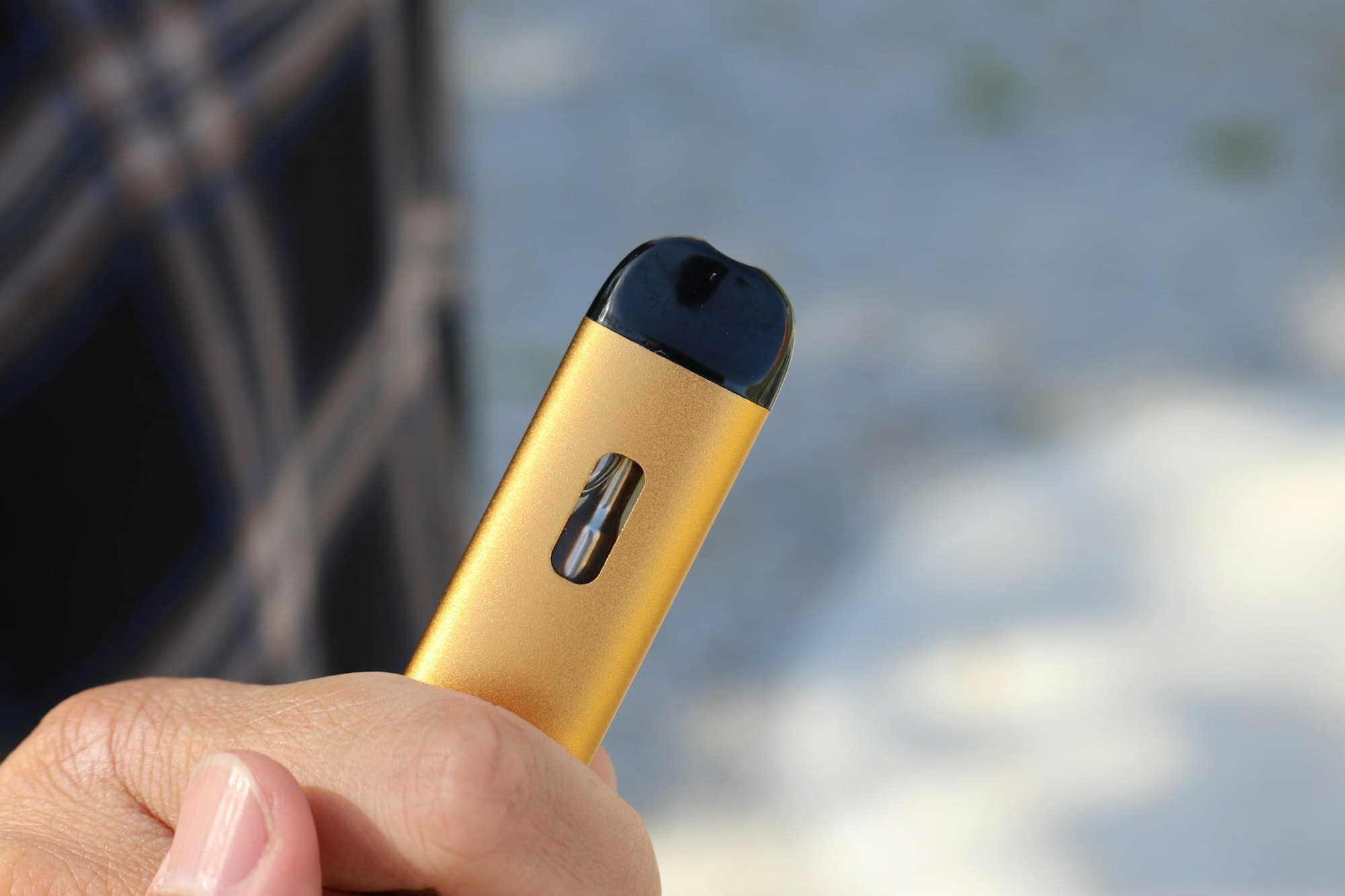 A person holding a compact rechargeable pod vape device outdoors, with a visible e-liquid window in the device body