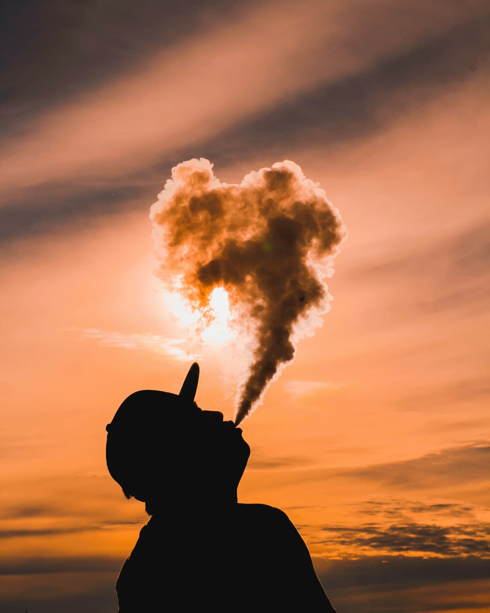 Silhouette of a person exhaling a dense cloud of vapour outdoors at dusk